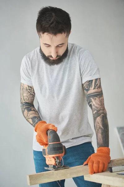 Handsome Bearded Tattooed Man Holding Wooden Plank Using Electric Jigsaw — Free Stock Photo