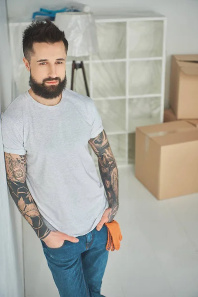 Pohledný Vousatý Tetovaný Muž Stojící Rukama Kapsách Novém Domě — Stock fotografie zdarma