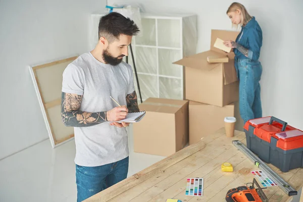 Bärtiger Mann Beim Notieren Und Junge Frau Beim Auspacken Von — kostenloses Stockfoto