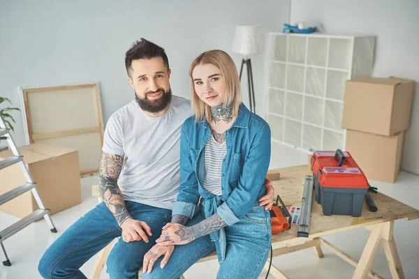 Šťastný Mladý Pár Tetování Sedí Pohromadě Usmívá Kameru Při Opravách — Stock fotografie zdarma