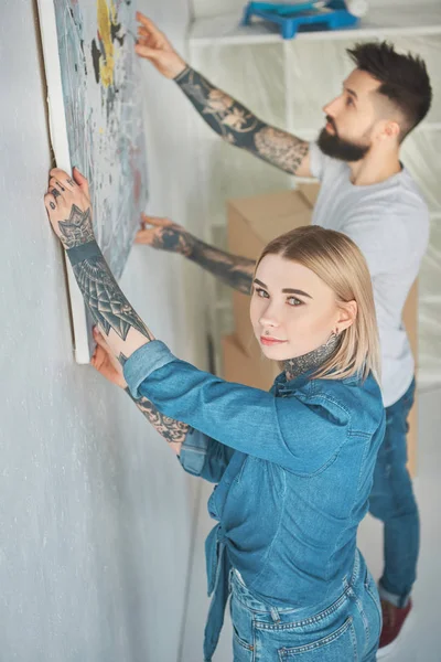 Jonge Getatoeëerd Paar Hangende Schilderij Aan Muur Bij Nieuwe Appartement — Stockfoto