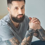 Retrato de homem barbudo com tatuagens olhando para a câmera