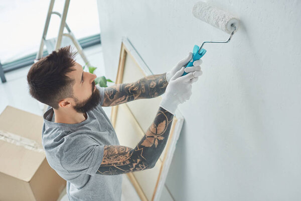 side view of tattooed repairman painting wall in new apartment