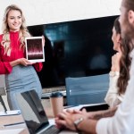 Smiling businesswoman showing tablet in hands to colleagues during meeting in office