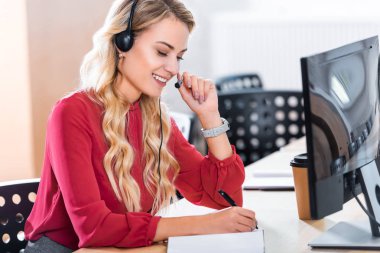 side view of beautiful female call center operator in headset at workplace in office clipart