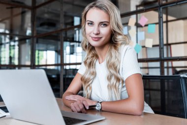 dizüstü bilgisayar kullanarak ve kamera Office gülümseyen güzel genç iş kadını
