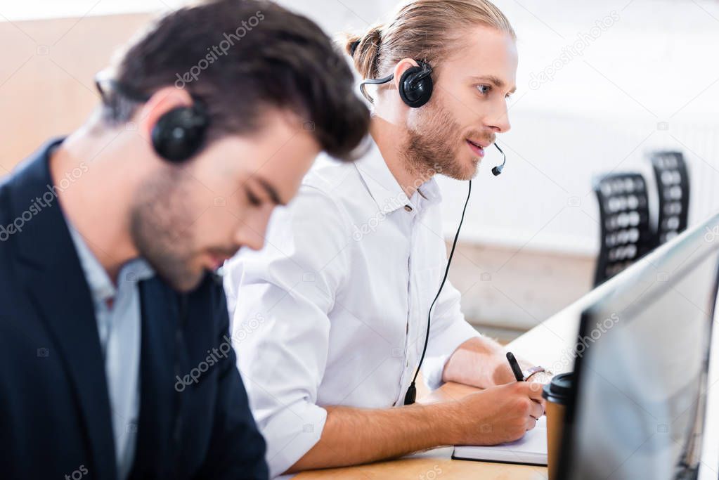 selective focus of male call center operators in headsets at workplace in office