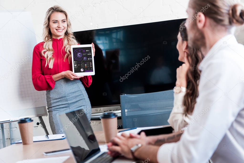 businesswoman showing tablet in hands to colleagues during meeting in office