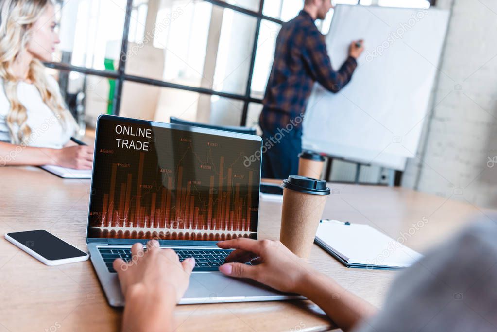 cropped cropped shot of business person using laptop with online trading website on screen during meeting with colleagues 