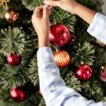 Imagen recortada de niño afroamericano en pijama decorando árbol de navidad con adornos en casa