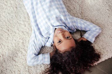 üstten görünüm gülümseyen sevimli Afro-Amerikan çocuk halı odasında yatarken pijama