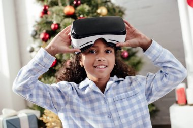 sanal gerçeklik kulaklık kullanarak ve Noel kavramı evde, kameraya bakarak pijama Afro-Amerikan çocuk
