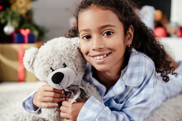可爱的快乐非洲裔美国儿童的肖像在睡衣与泰迪熊在家看相机 — 图库照片