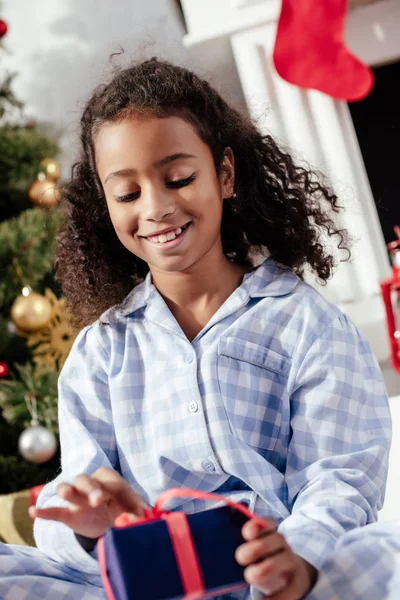 自宅のクリスマスのギフトを開くパジャマ姿で愛らしいアフリカ系アメリカ人子供の選択と集中  — 無料ストックフォト