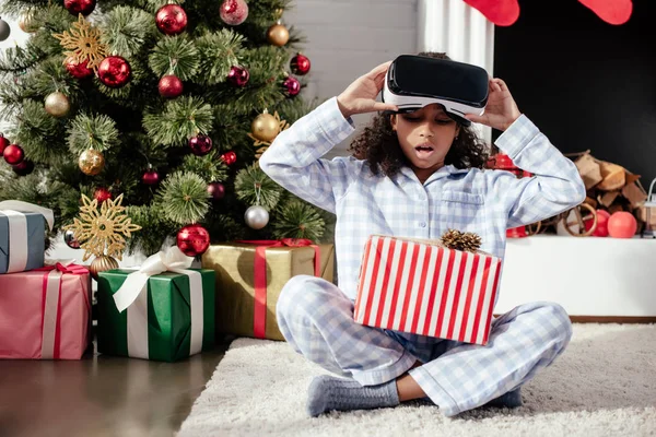 惊讶可爱的非洲裔美国人的孩子在睡衣和虚拟现实耳机看圣诞节礼物在家 — 图库照片