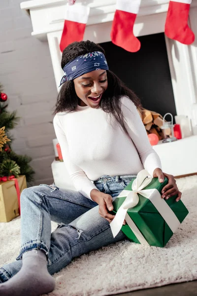 惊讶迷人的非洲裔美国妇女在家看圣诞节礼物 — 免费的图库照片