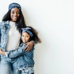 Portret van stijlvolle Afro-Amerikaanse moeder en dochter in soortgelijke kleding poseren op muur thuis
