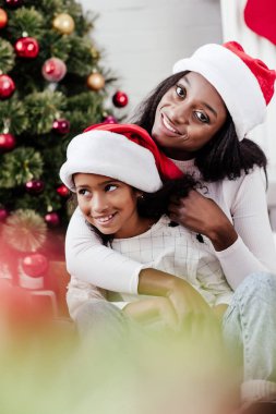 Afrika kökenli Amerikalı anne Noel Baba şapkalı bir şekilde dekore edilmiş oda evde küçük kızını sarılma
