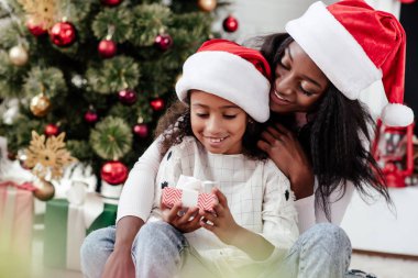 mutlu Afrikalı-Amerikalı kadın ve Hediyelik Noel Baba'ya kızıyla şapka evde, newy yıl ve Noel kavramı