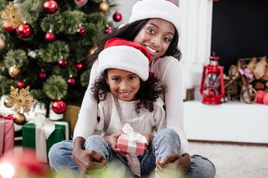 mutlu Afrikalı-Amerikalı kadın ve Hediyelik Noel Baba'ya kızıyla şapka evde, newy yıl ve Noel kavramı