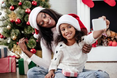 Afro-Amerikan aile içinde Smartphone cep telefonu ile dekore edilmiş oda evde, Noel tatil kavramı içinde selfie alarak Noel Baba şapkaları