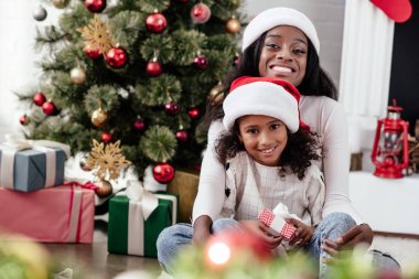 mutlu Afrikalı-Amerikalı kadın ve Hediyelik Noel Baba'ya kızıyla şapka evde, newy yıl ve Noel kavramı
