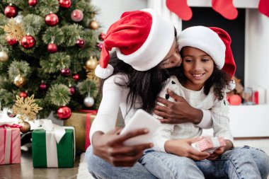 Afro-Amerikan aile içinde Smartphone cep telefonu ile dekore edilmiş oda evde, Noel tatil kavramı içinde selfie alarak Noel Baba şapkaları