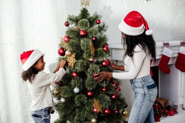 Afrika kökenli Amerikalı anne ve kızı Noel Baba'ya şapka dekorasyon Sunni Noel ağacı birlikte evde