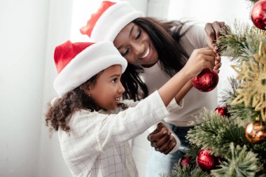 Afrika kökenli Amerikalı anne ve kızı Noel Baba'ya şapka dekorasyon Sunni Noel ağacı birlikte evde