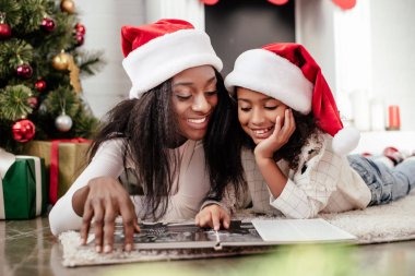 Afro-Amerikan aile Noel Baba şapkaları evde Noel için dekore edilmiş oda fotoğraf albümünüzde bakarak içinde gülümseyen