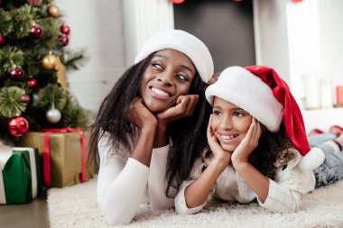 Afro-Amerikan ailesinde neşeli Noel için dekore edilmiş oda katta evde yatan Noel Baba şapkaları