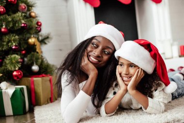 Afro-Amerikan ailesinde neşeli Noel için dekore edilmiş oda katta evde yatan Noel Baba şapkaları