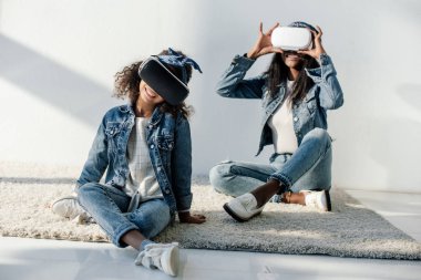 african american mother and daughter in similar clothing and vr headsets at home clipart