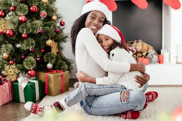 Lycklig Afroamerikanska Kvinna Och Dotter Santa Claus Hattar Kramas Inredda — Stockfoto