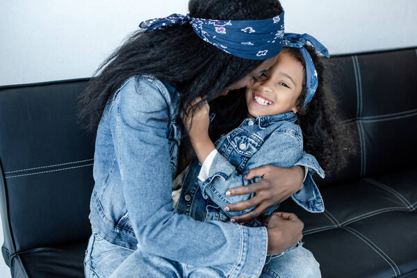 african american woman and cheerful daughter having fun on sofa at home