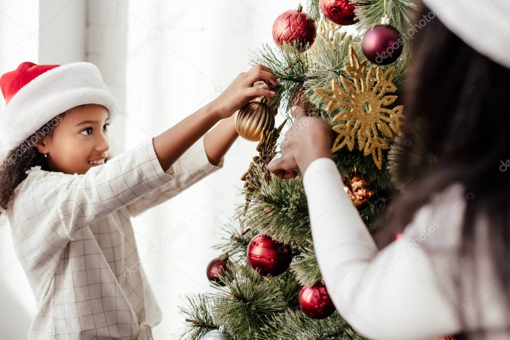 partial view of african american woman and kid decorating christmas tree together at home