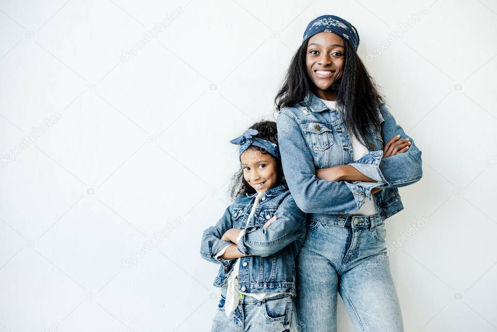 stylish african american mother and daughter in similar clothing posing at wall at home