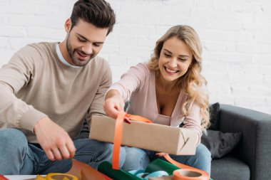 smiling couple preparing christmas gift box together at home clipart