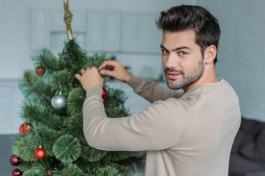 baubles ile Noel ağacı süsleme ve kameraya evde seyir yakışıklı adam