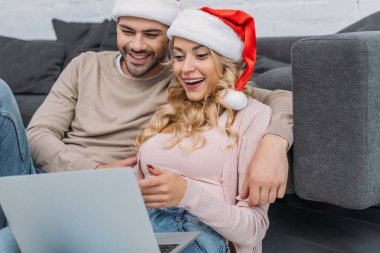heyecanlı kaç Noel Baba şapkaları kanepe yakınındaki dizüstü evde kullanma içinde
