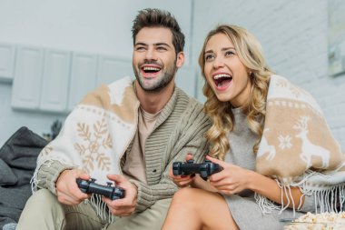 beautiful young couple playing video games and having fun together on couch at home clipart