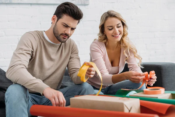 Cheerful Couple Preparing Christmas Gift Box Together Holding Ribbons Home — Free Stock Photo