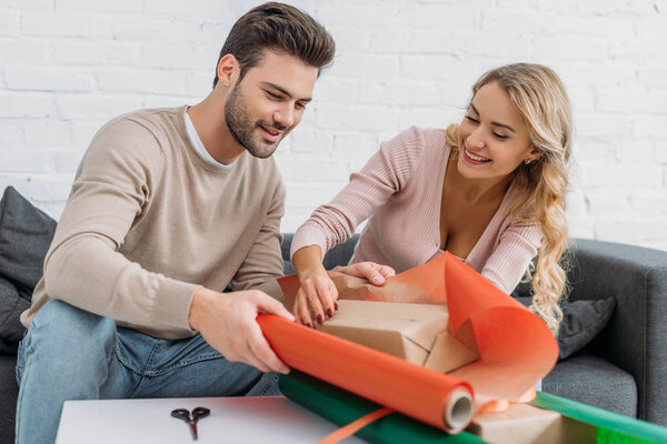 happy couple preparing christmas gift box together at home