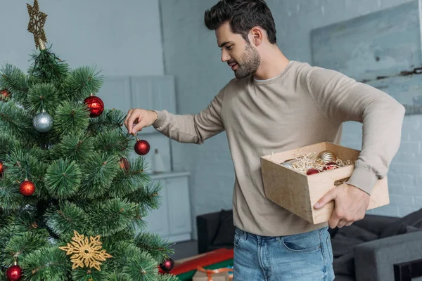 Homem Bonito Decorando Árvore Natal Com Bugigangas Segurando Caixa Madeira — Fotografia de Stock