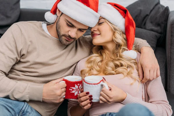 Couple Affectueux Dans Santa Chapeaux Tenant Tasses Cappuccino Maison — Photo