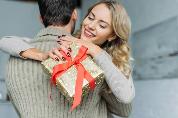 美丽的女孩与礼物盒拥抱她的男朋友在家 — 图库照片