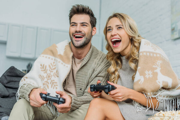 красивая молодая пара играет в видеоигры и весело проводит время вместе на диване дома
