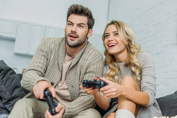улыбающаяся молодая пара, играющая вместе в видеоигры на диване дома

