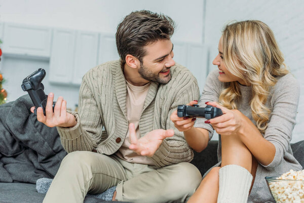 счастливая молодая пара играет в видеоигры вместе на диване дома
