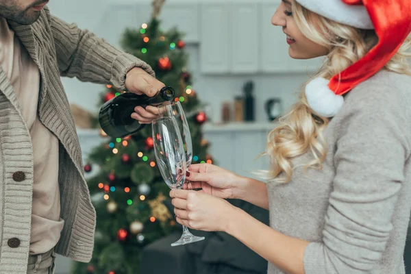 年轻夫妇的短拍在家里的圣诞树前倒入香槟到玻璃杯 — 免费的图库照片